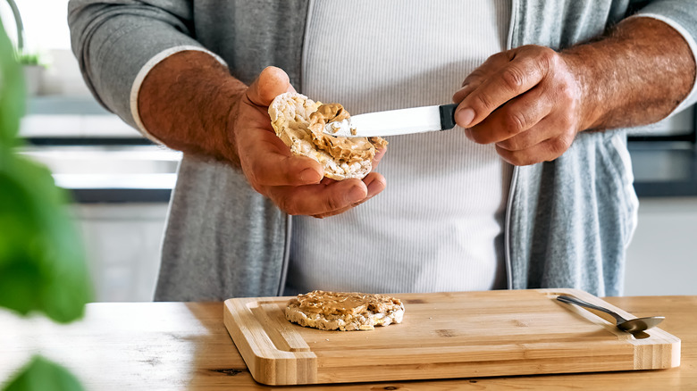Person smearing peanut butter onto rice cakes for a healthy breakfast.