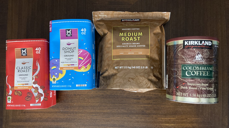 Sam's Club and Costco ground coffees in canisters and packages on table, including Member's Mark Donut Shop and Kirkland Signature Colombian