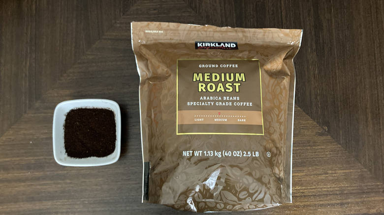 Package of Kirkland Signature medium roast ground coffee next to ramekin of ground coffee