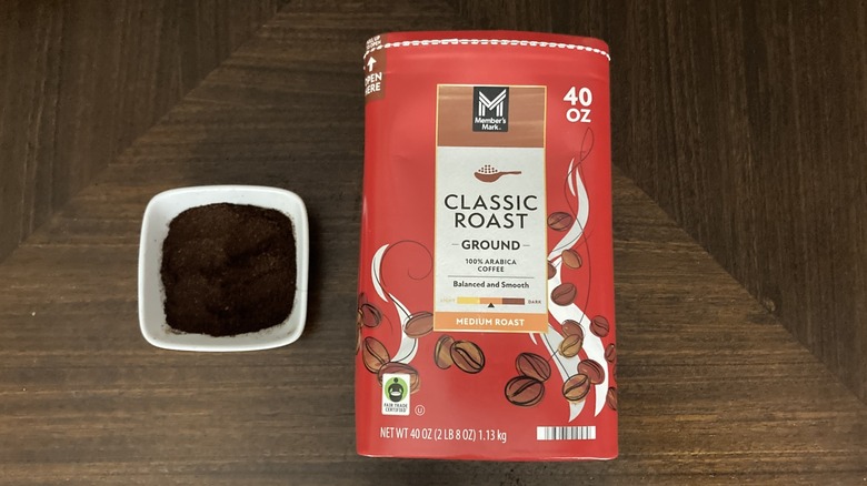 Cardboard canister of Member's Mark classic medium roast ground coffee next to ramekin of coffee grounds