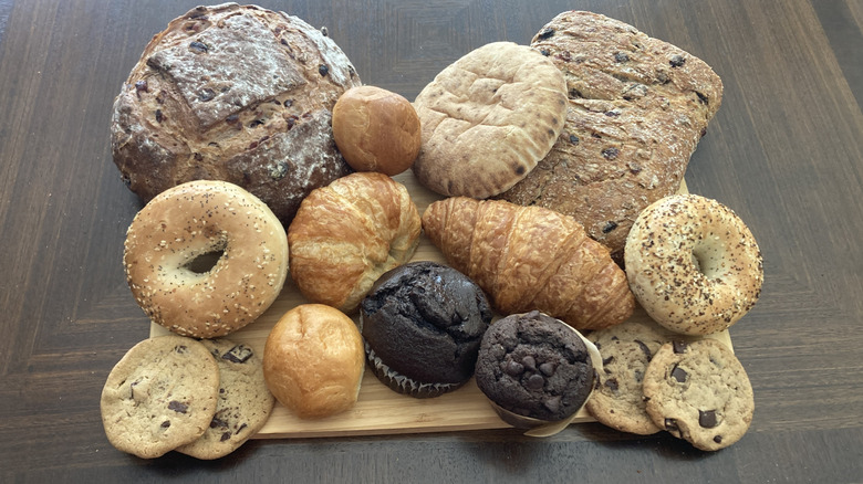 A variety of baked goods including bread, cookies, muffins, and bagels on a wooden table