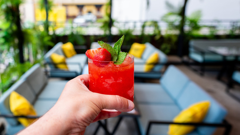 Hand holding strawberry cocktail with outdoor seating in background