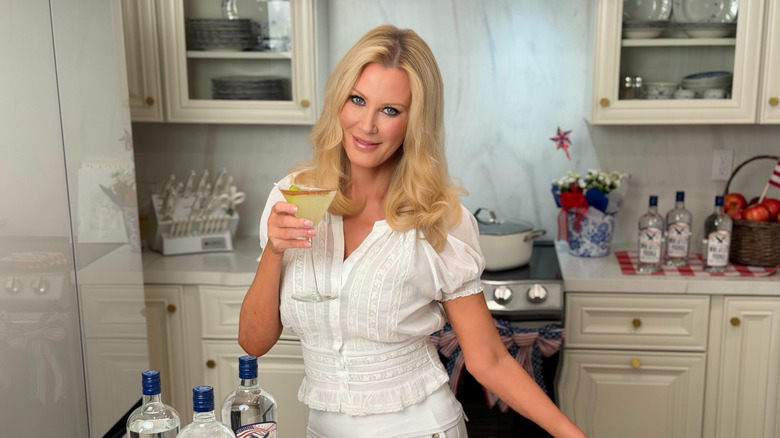 Sandra Lee standing in a kitchen, posing with a drink, looking into the camera