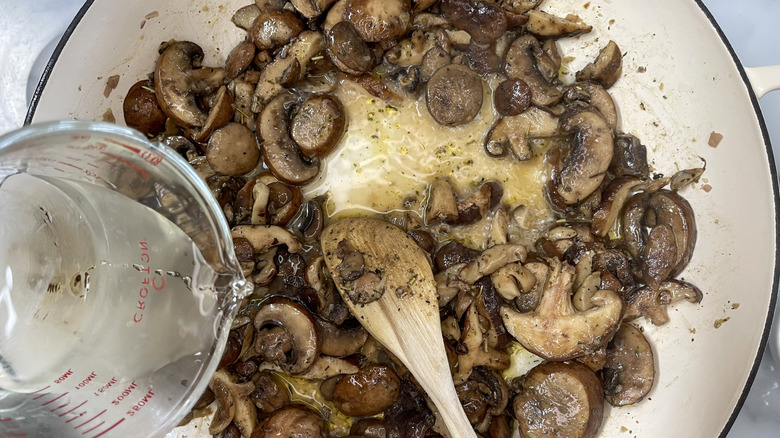 cup of pale liquid hovering over pot of mushrooms