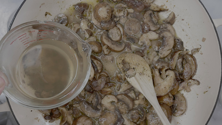 cup of slightly darker liquid hovering over pot of mushrooms