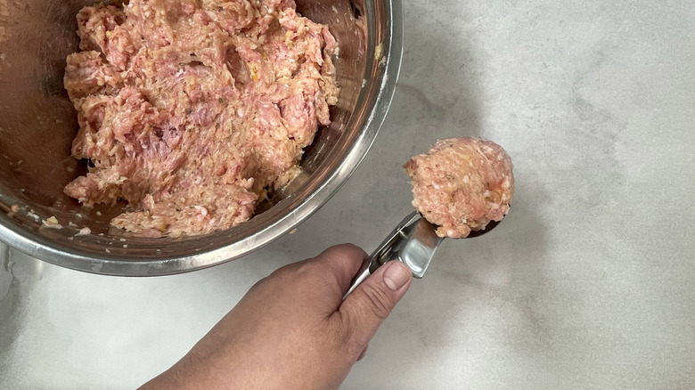 hand holding meatball in metal scoop