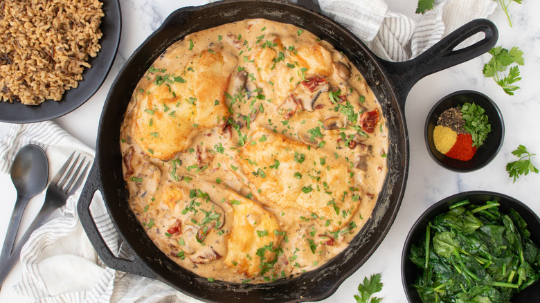 Skillet chicken in mushroom sauce next to greens and bowl of spices