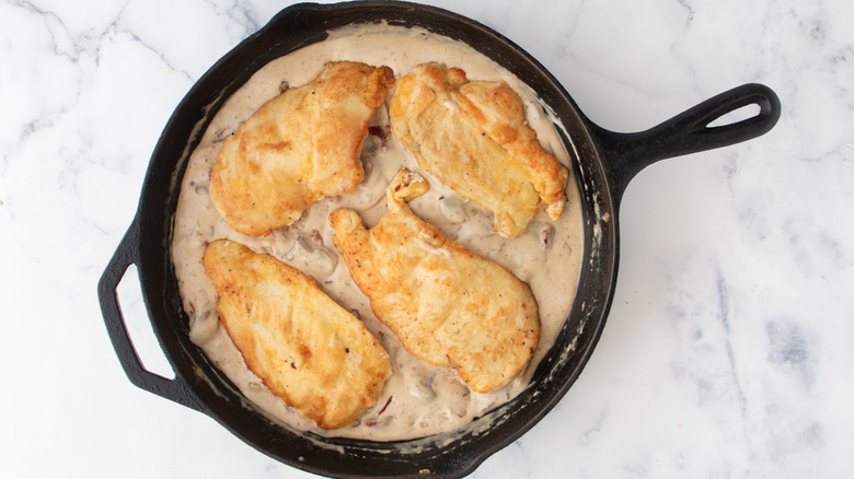 chicken breasts cooking in skillet with vegetables and sauce