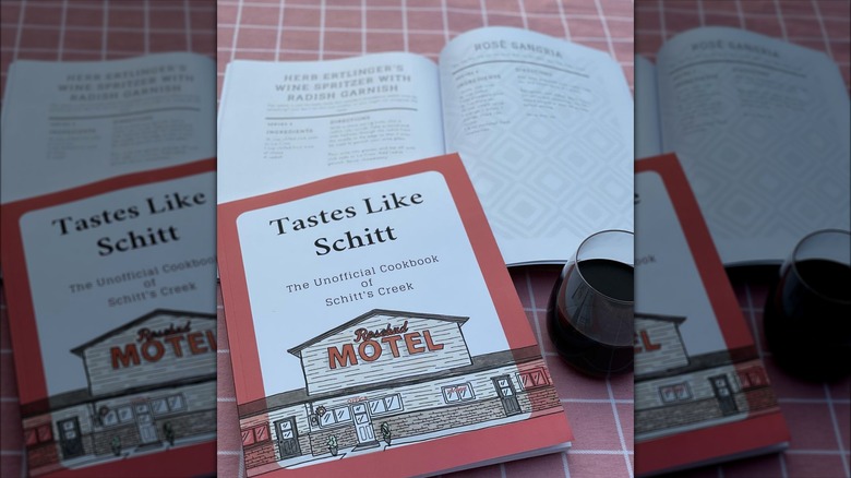 The Tastes Like Schitt cookbook beside glass of wine