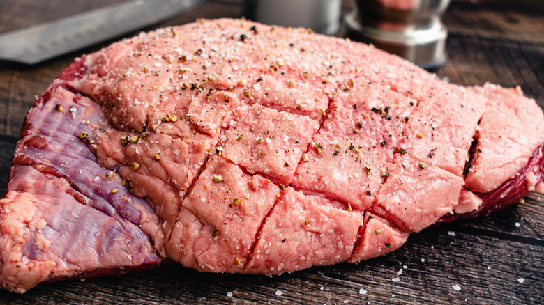 Raw, scored steak up close on wooden table with knife and other metal objects in background