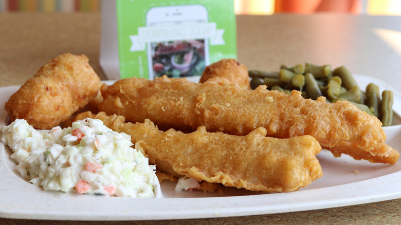 Plate of battered fish with potato salad and green beans on restaurant table.