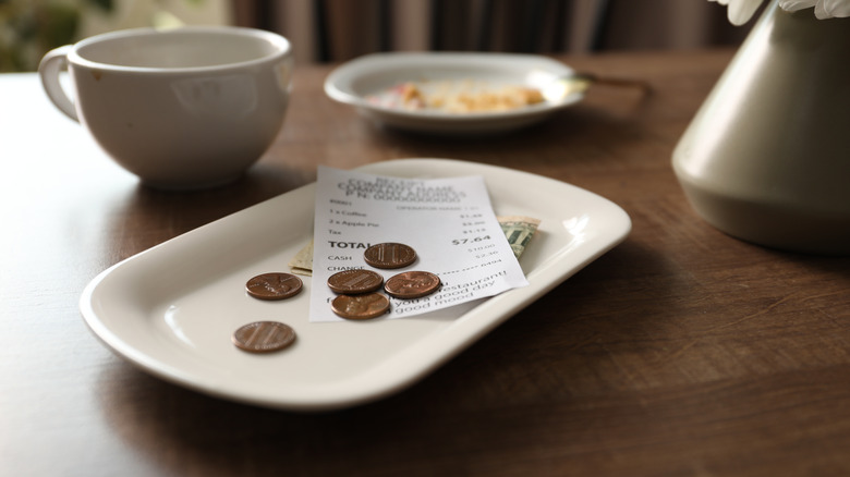 A white tray with a receipt, dollar bills, and some coins on a table