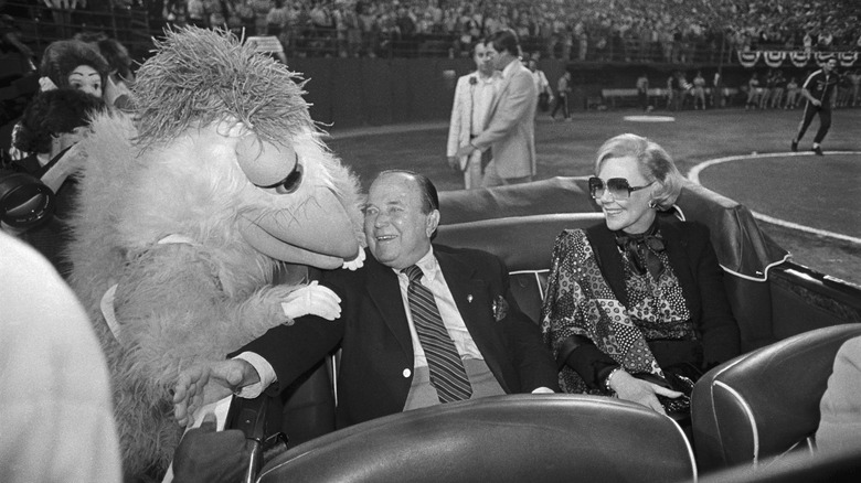 A black and white photo of Ray Kroc with the San Diego Chicken mascot at a baseball game