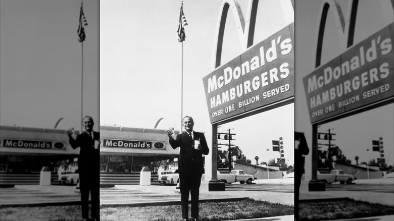 A black and white photo of Ray Kroc posing in front of a McDonald's