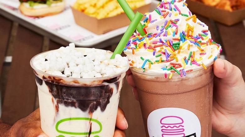 Two Shake Shack milkshakes with burgers and fries in the background