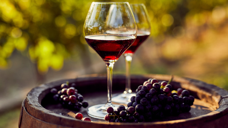 Two glasses of red wine on barrel with grapes.