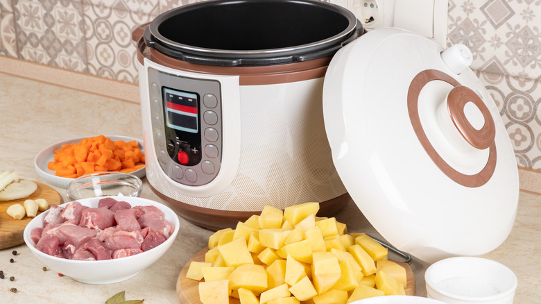 White pressure cooker on countertop with chopped meat and veggies