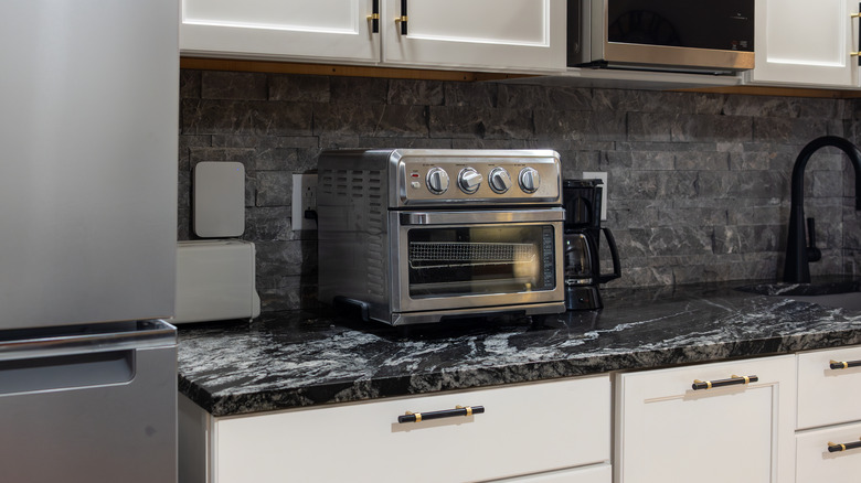 Toaster oven on dark marble countertop with stone backsplash