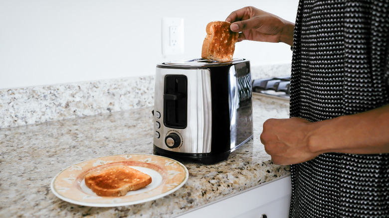 Person removing toasted bread from toaster