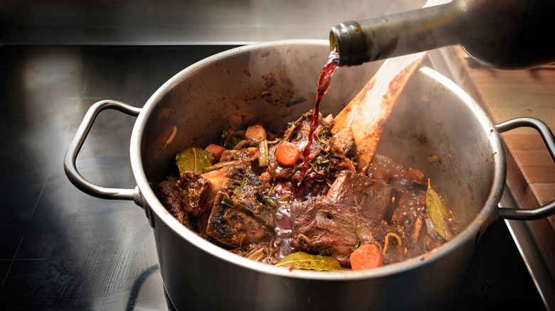 Red wine being poured into a pot of beef stew