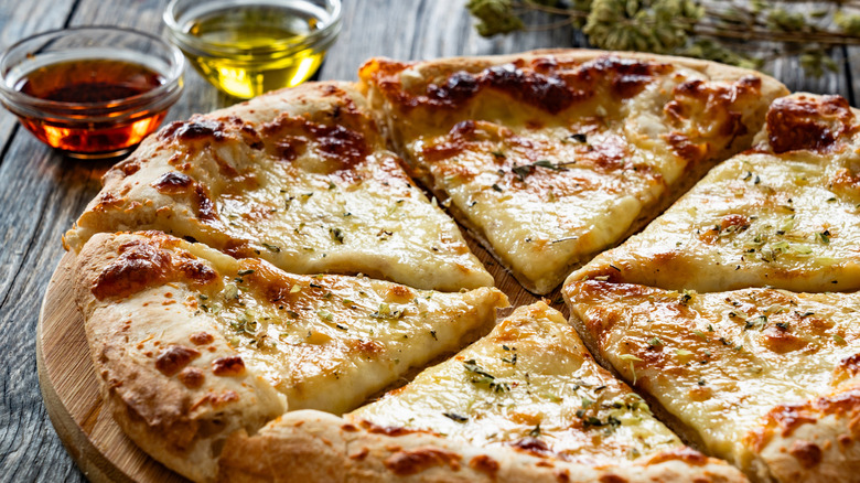 Freshly cooked pizza cut into slices on wooden cutting board
