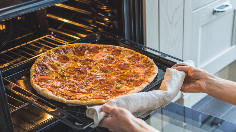 Person taking cooked pizza out of the oven