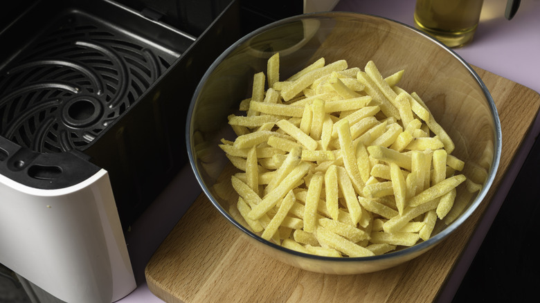 Frozen fries in a glass bowl beside an air fryer basket