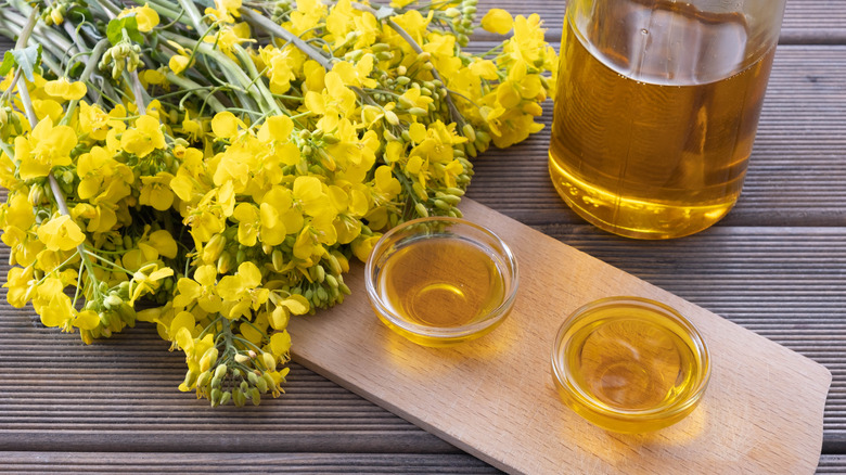 Small bowls of canola oil on cutting board with yellow flowers nearby.