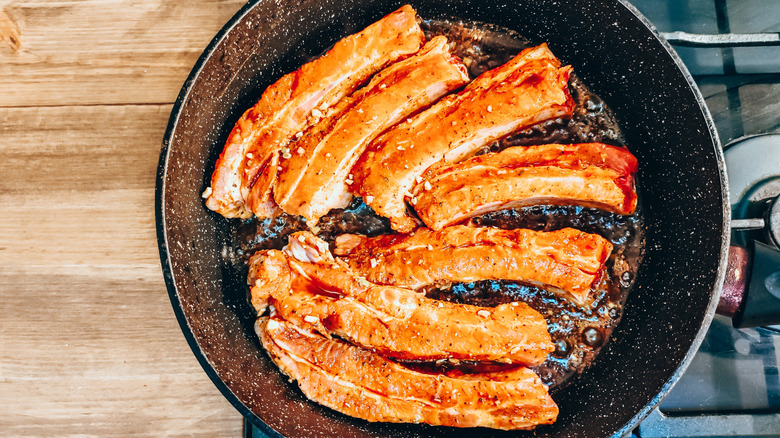 Pork ribs cooking in pan on stovetop next to wooden counter