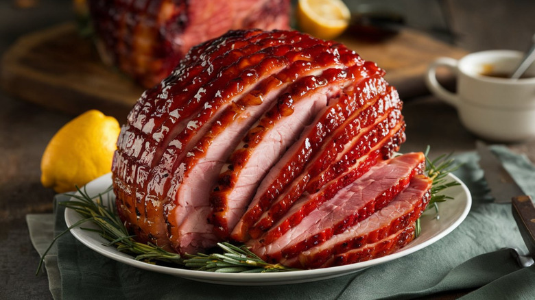 A glazed baked ham, partially sliced, on serving plate