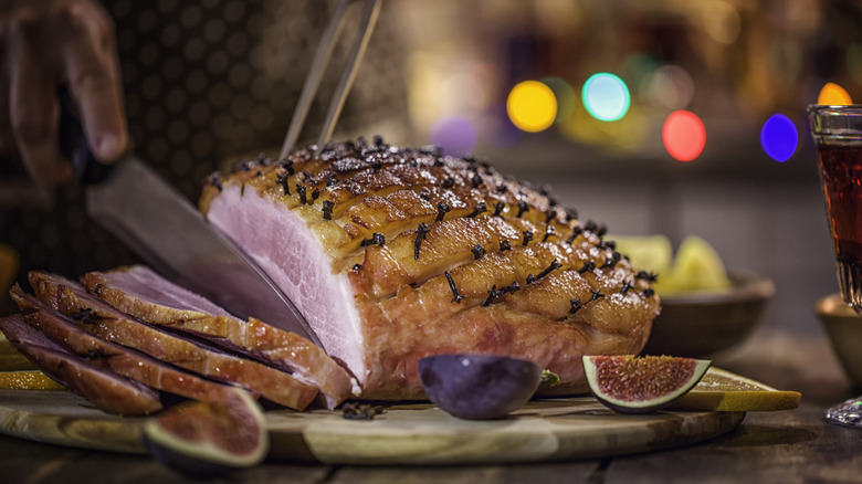Person carving a baked holiday ham on cutting board