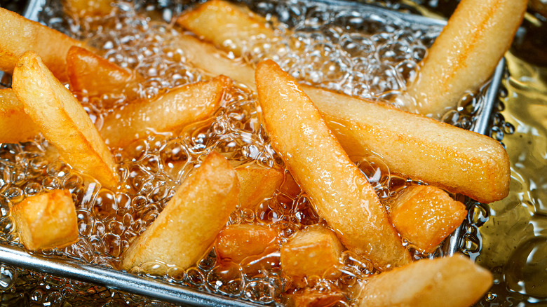 A close up to golden french fries frying in oil 