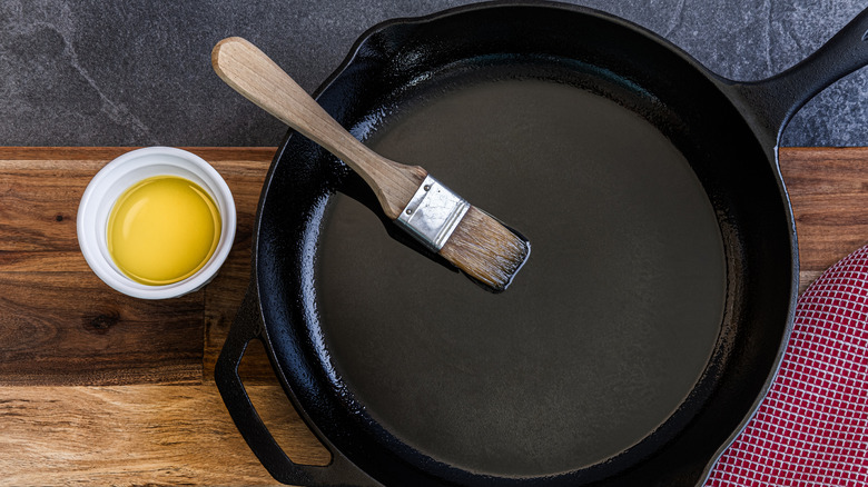 Small bowl of oil and brush with cast iron skillet on wood surface.