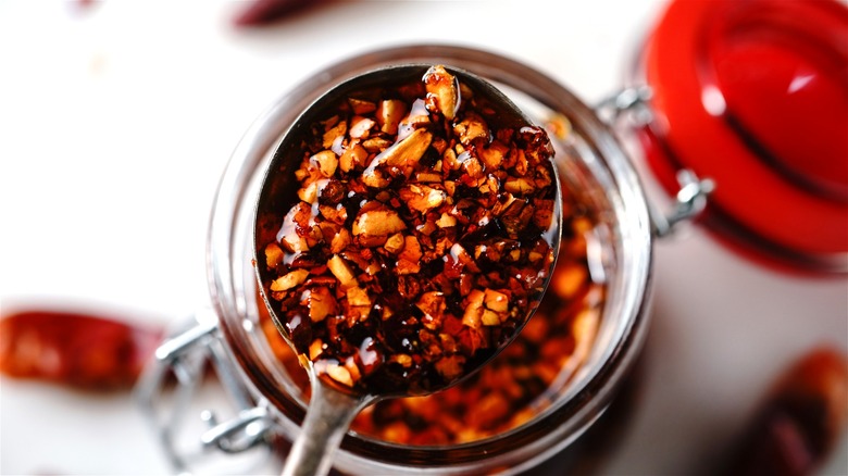 A close-up shot of a spoonful of chili crisp being scooped out from the jar.