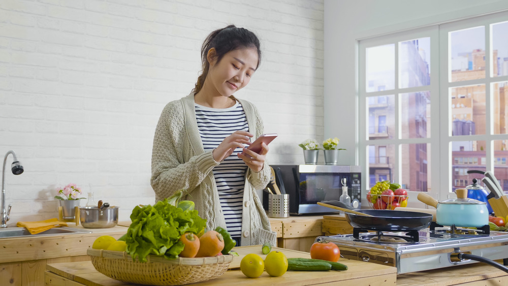 woman cooking with vegetables smartphone