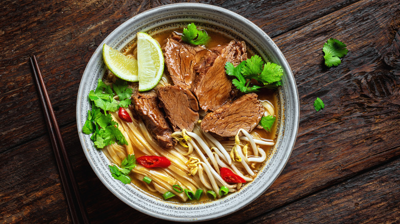Bowl of ramen with sliced meat, lime wedges, cilantro, and bean sprouts.