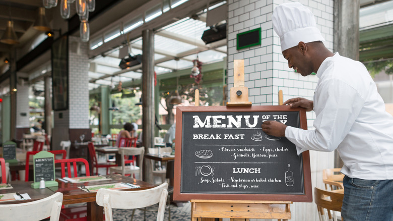 man writing restaurant specials on board