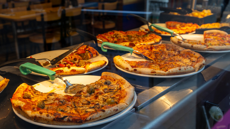 Multiple pizzas and serving utensils at buffet