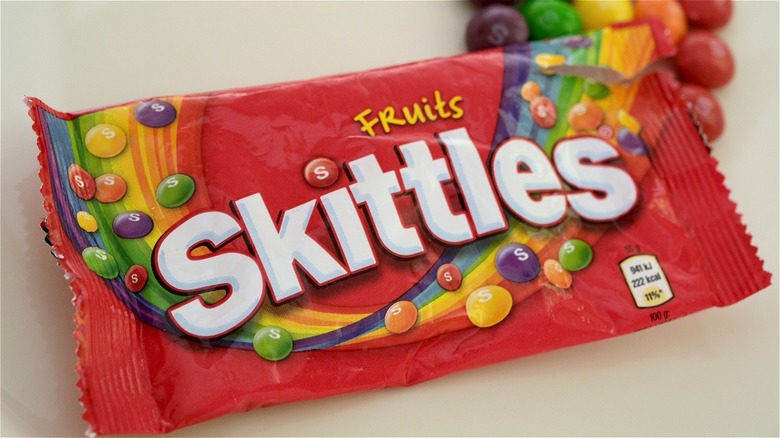A bag of Skittles with candy coming out of the edge