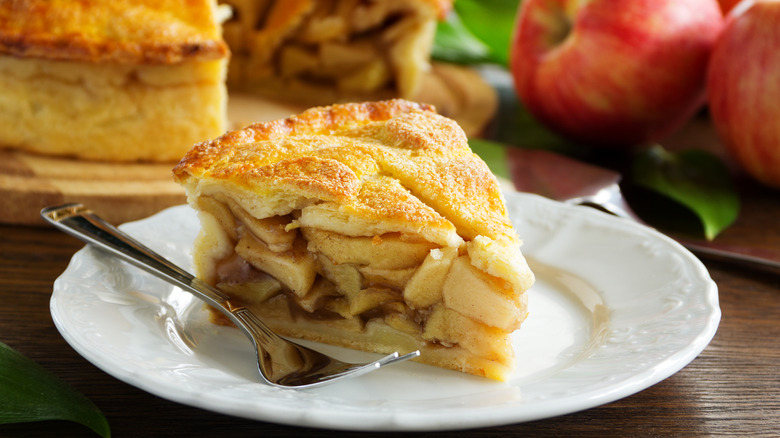 A slice of apple pie on a white plate with a fork