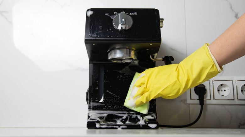 Hand in yellow rubber glove cleaning coffee machine