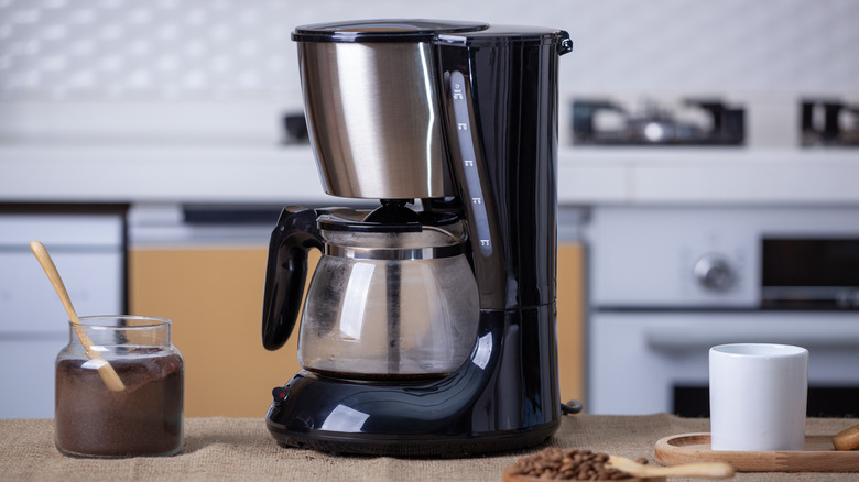 Coffee maker on counter with ground coffee and mug