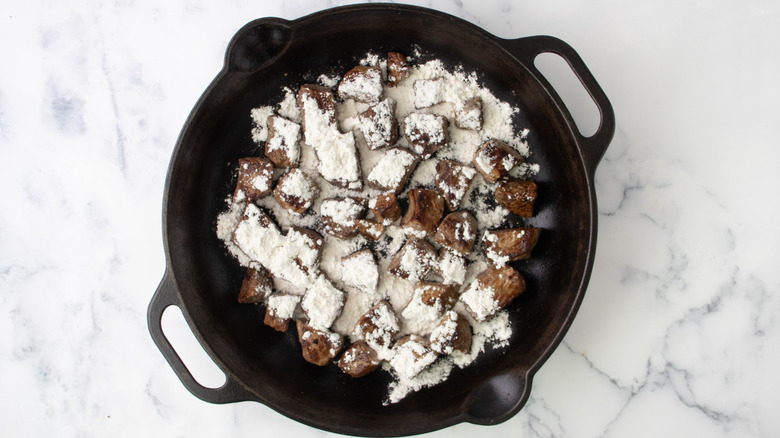 flour sprinkled in pan with seared steak cubes