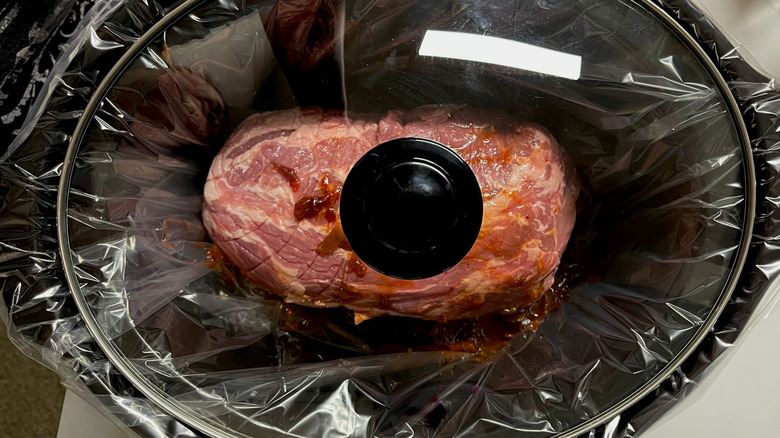 Pork butt roast in lined slow cooker with lid on
