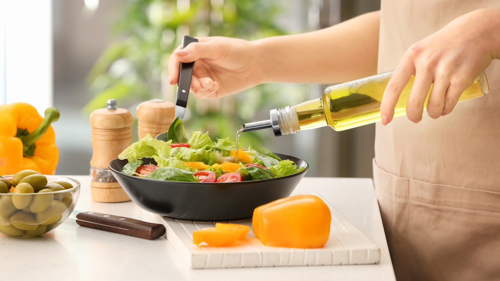 woman pouring olive oil on salad