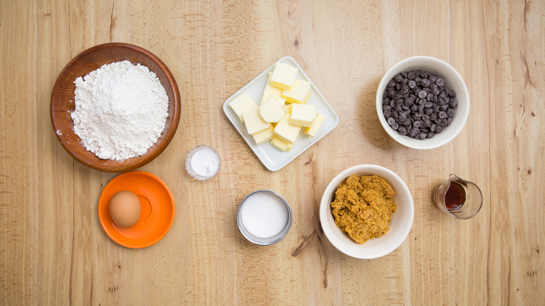 egg, cubes of butter, bowl of chocolate chips, and other cookie ingredients on table