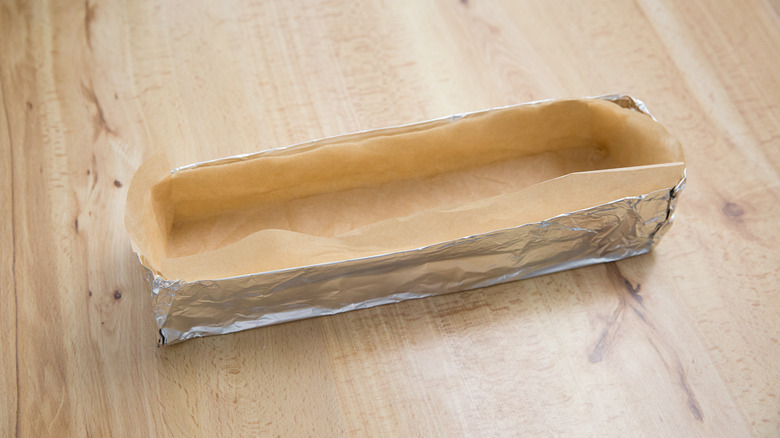 Makeshift rectangular aluminum foil pan lined with parchment paper on table
