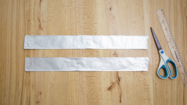 folded sheets of aluminum foil on table next to scissor and ruler