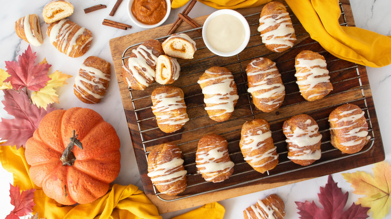Glazed pumpkin crescent rolls on wooden board surrounded by pumpkin and leaves