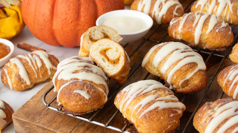 Glazed pumpkin crescent rolls next to pumpkin and bowl of cream cheese glaze